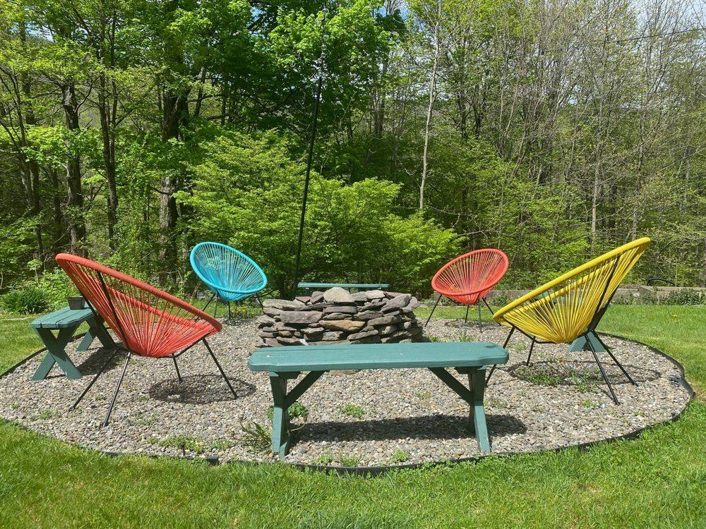 Outdoor stone fire pit surrounded by colorful Acapulco chairs and picnic benches