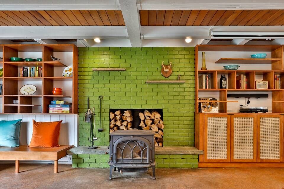 Living room with wood-burning stove set into a green brick fireplace, built-in wood shelving on either side
