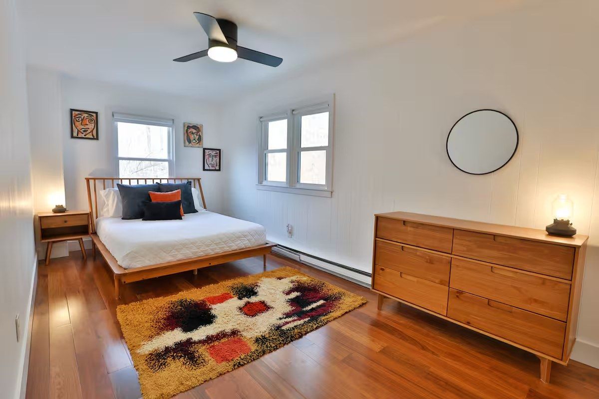 Primary bedroom with mid-century bed frame, walnut dresser, and round mirror