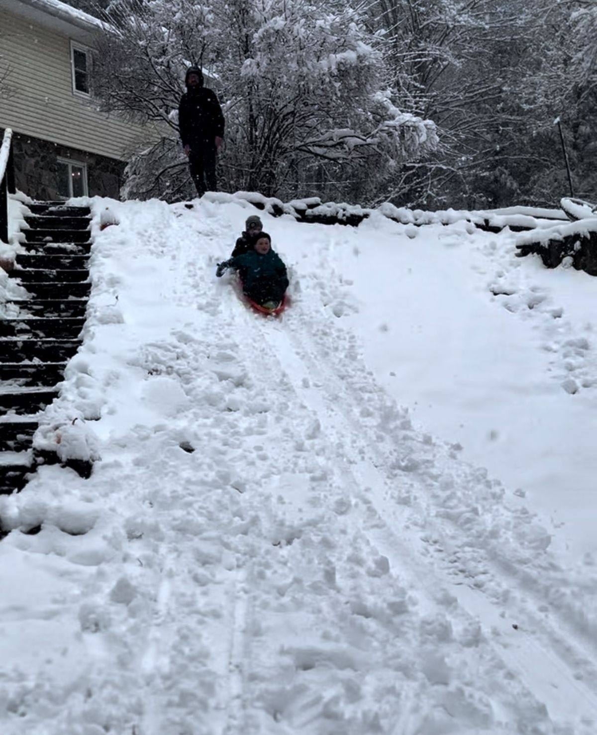 Kids sledding down the snow-covered front hill of the ski house
