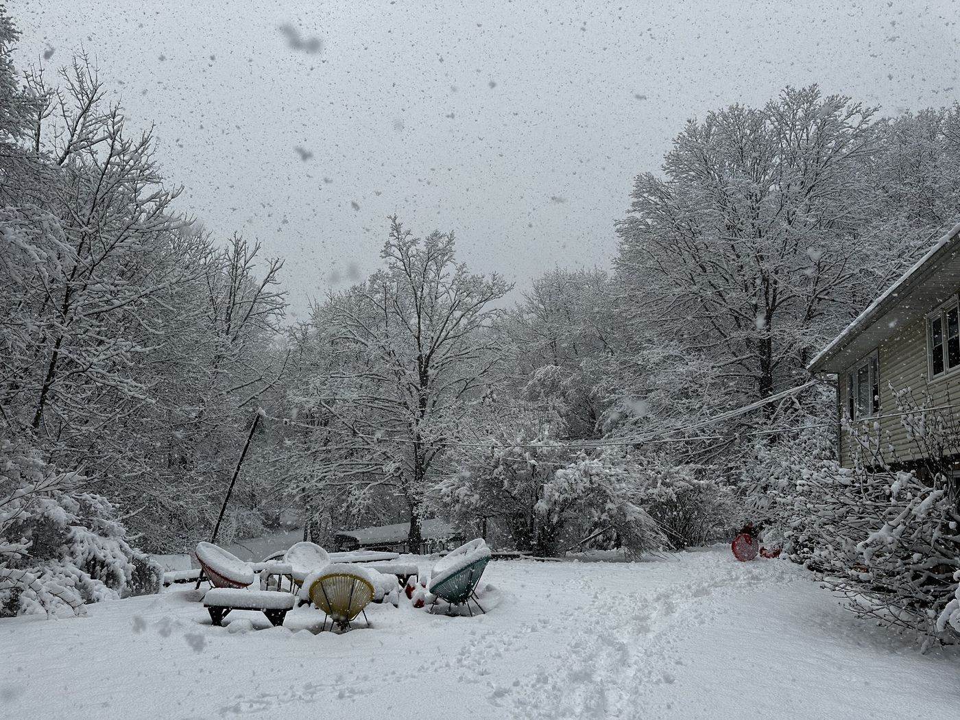 Snow-covered fire pit chairs during a winter storm