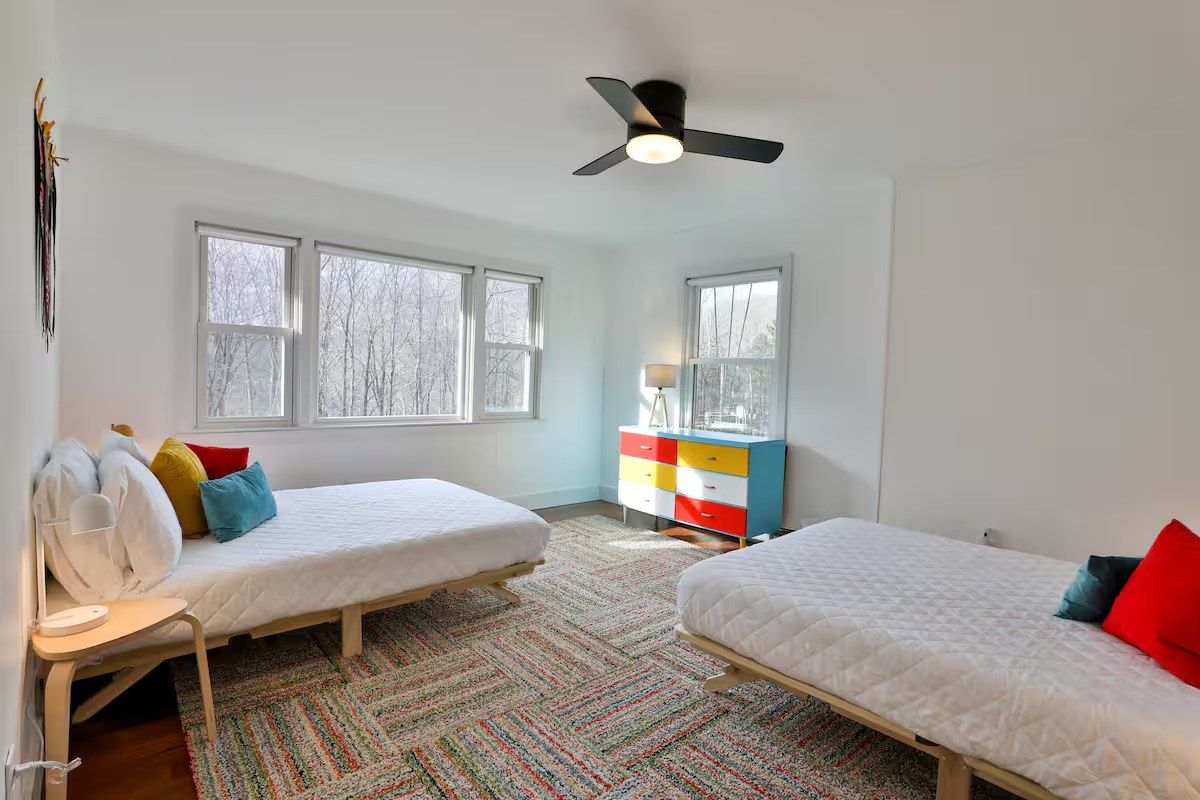 Twin bedroom with two beds and colorful pillows, striped rug, and a mid-century dresser